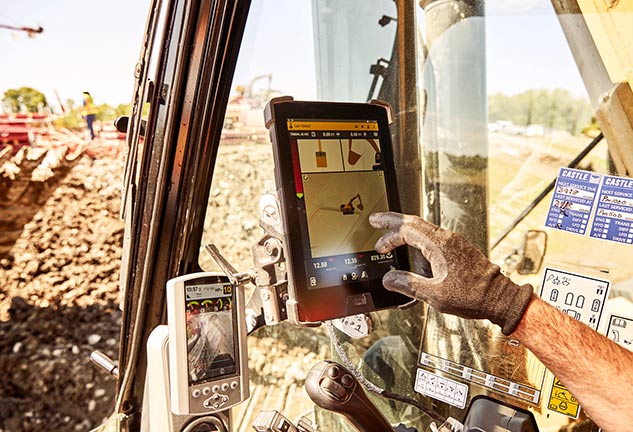 A gloved hand uses a screen to control construction equipment on a job.