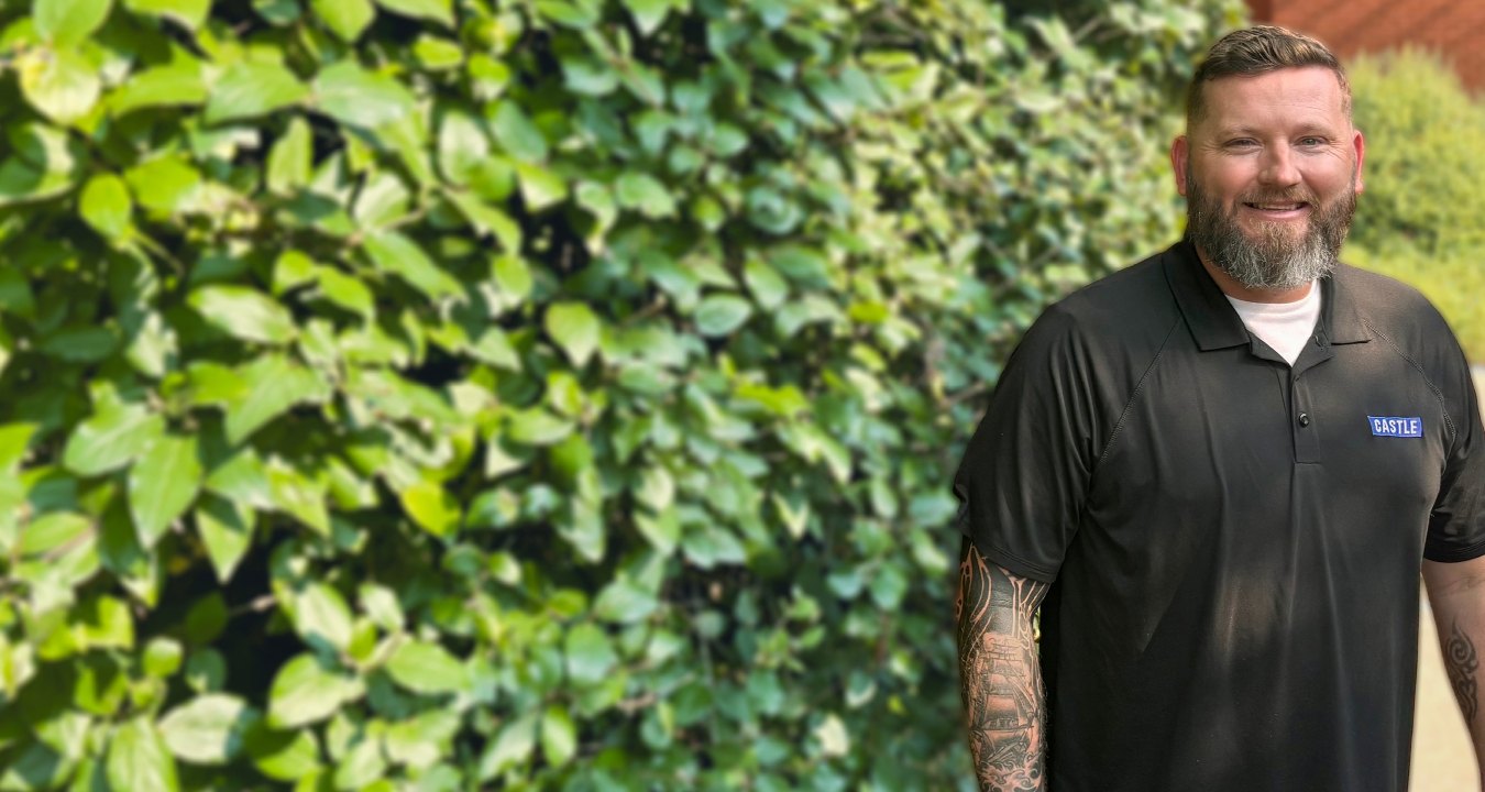 Pennington in black polo standing in front foliage smiling at camera