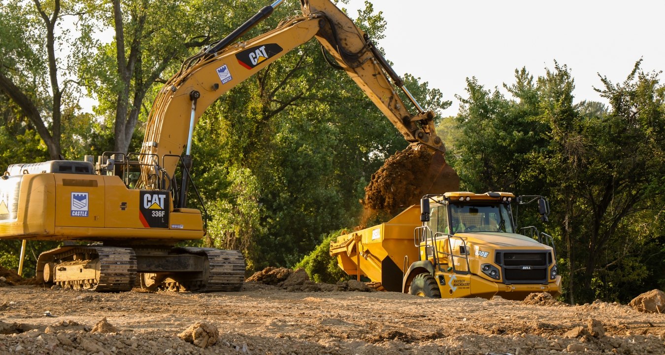 Yellow CAT excavator pouring dirt into yellow dump truck bed
