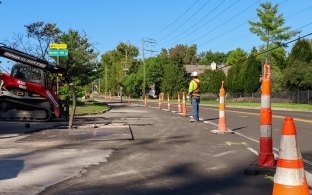 orange traffic cones, construction worker, and excavation machines on residential road