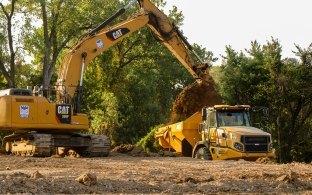 Yellow CAT excavator pouring dirt into yellow dump truck bed