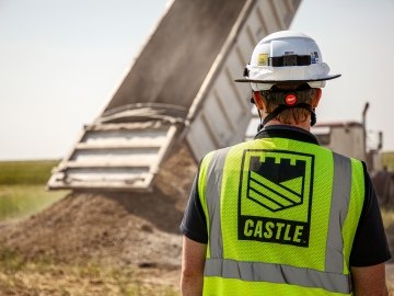 Construction worker in Castle PPE in front of dump truck