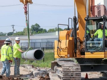 Two people working next to a piece of equipment and one person operating the equipment.