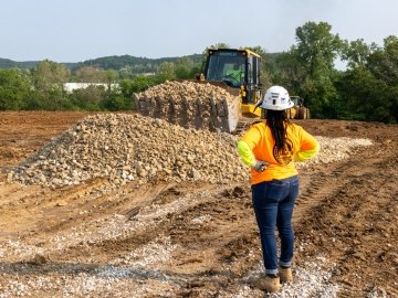 Woman construction worker watching bulldozer move rock pile