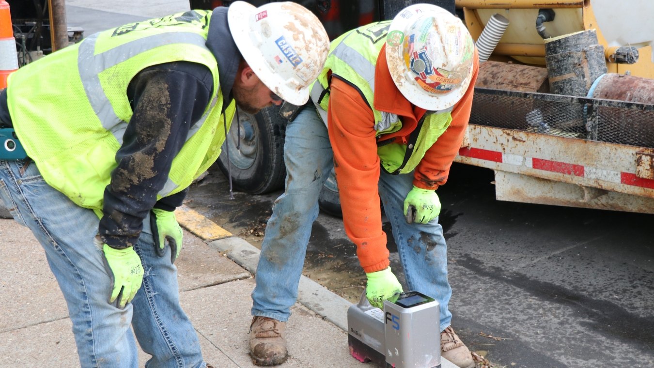 Two construction workers in PPE measuring directional boring pipe depth