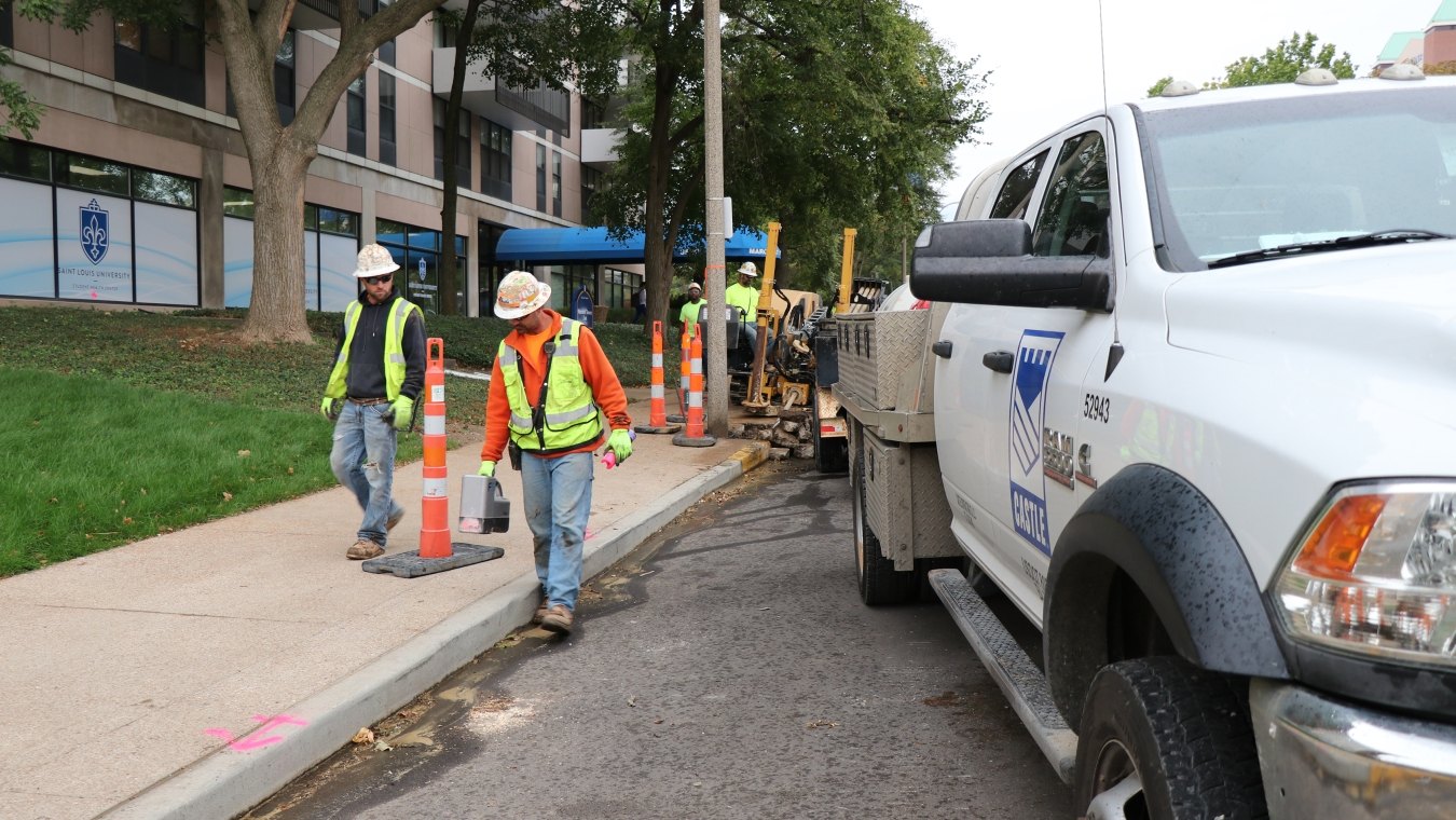 Construction workers walking along a straight line and using hand-held device to measure underground directional boring pipe