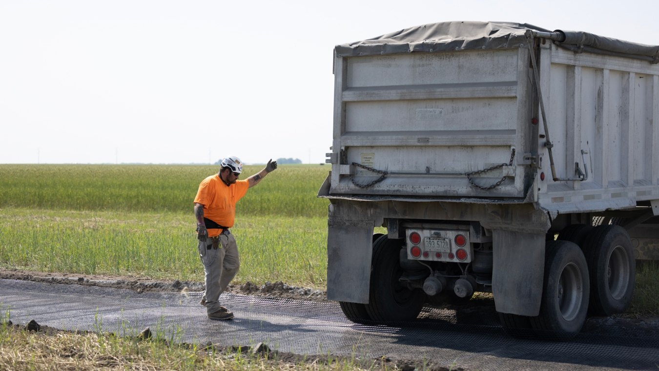 Construction worker directing dump trunk reversing into position