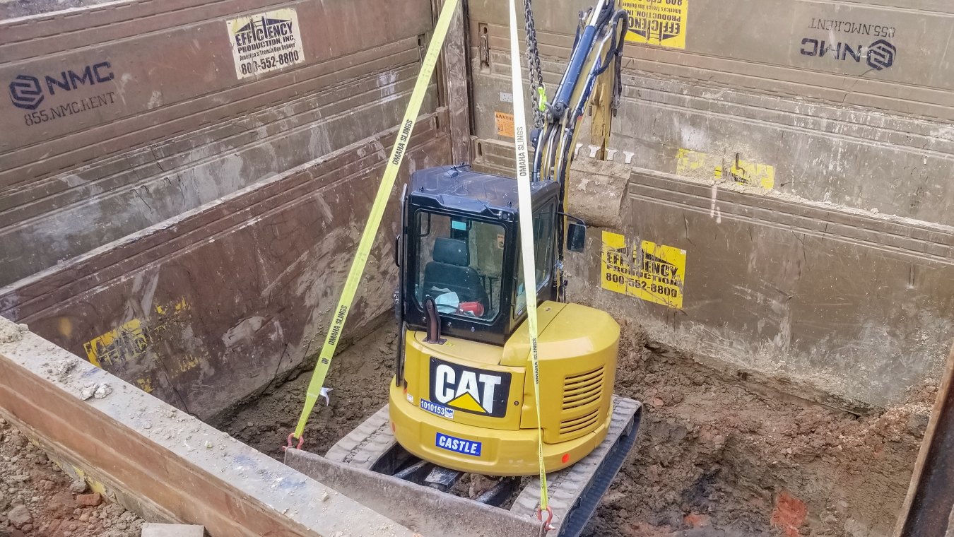 CAT yellow excavator lowered in utilities pit