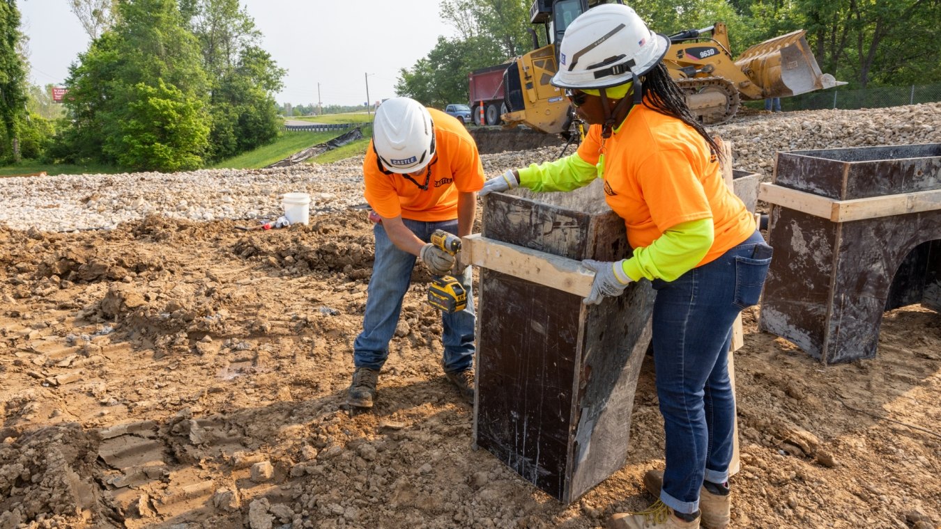 Woman construction worker holding wood panels together and man construction worker drilling wood through wood panels