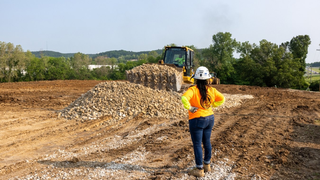 Woman construction worker watching bulldozer move rock pile