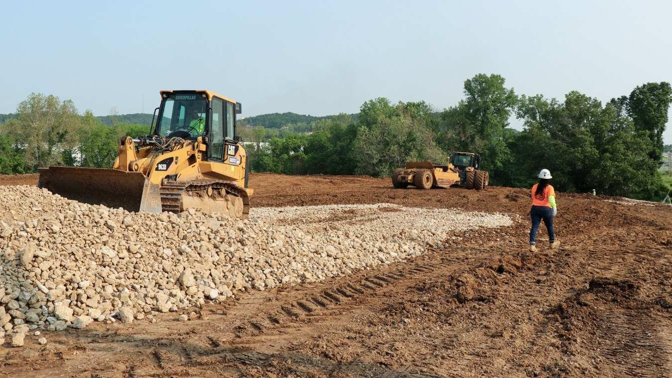 Woman construction worker walking past bulldozer moving rock pile