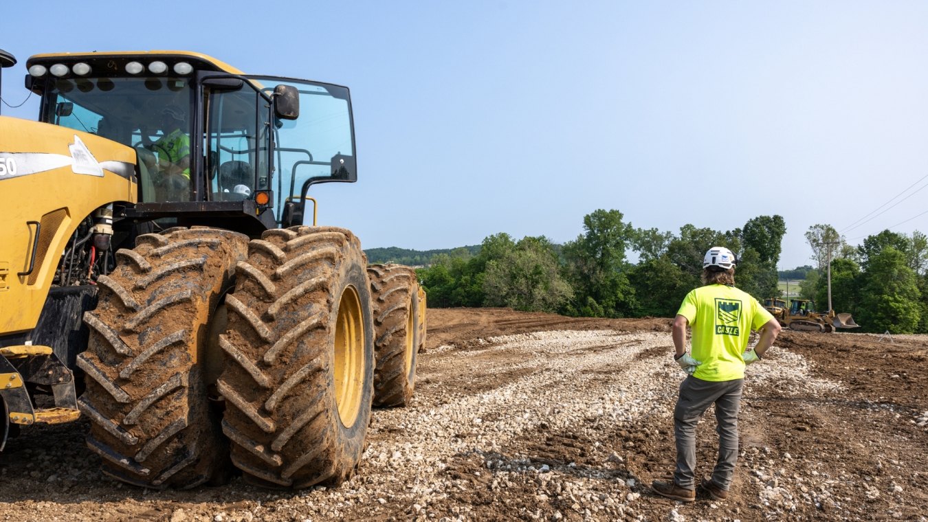 Castle Contracting construction worker next to large yellow tractor looking out across construciton site landscape