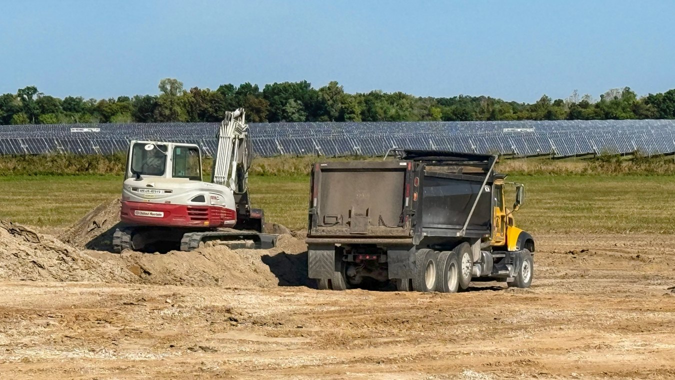 Dump truck and excavator facing solar panels in field