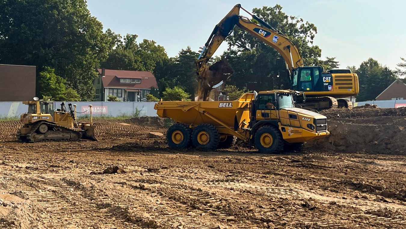 Mini dozer with CAT excavator dropping dirt into yellow John Deer dump truck