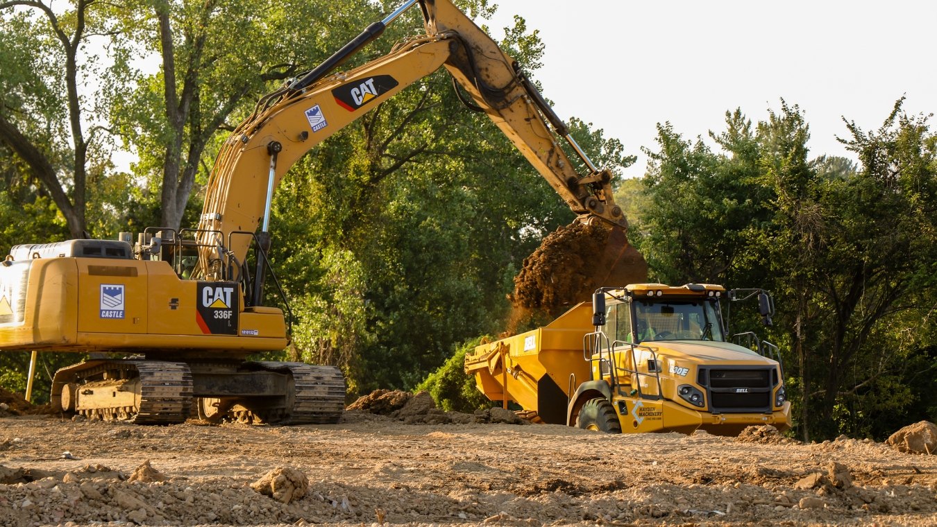 Yellow CAT excavator pouring dirt into yellow dump truck bed