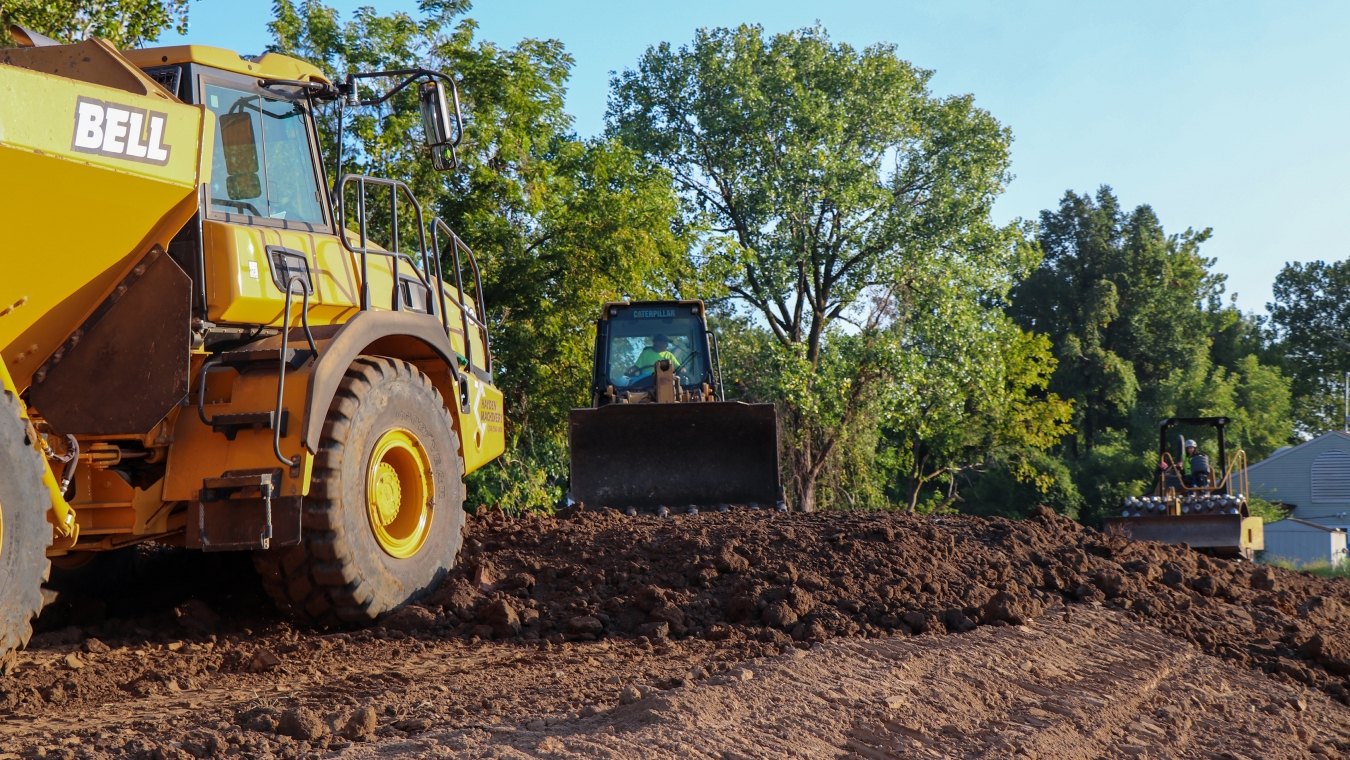 Yellow John Deer dump truck facing dozer on project site