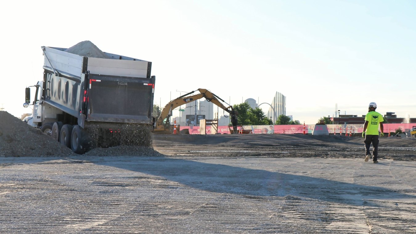 Dump truck, excavator and construction worker on construction site with the St. Louis city skyline in the background