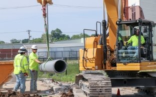 Two people working next to a piece of equipment and one person operating the equipment.