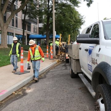 Construction workers walking along a straight line and using hand-held device to measure underground directional boring pipe