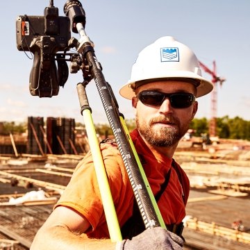 Castle Contracting construction worker in PPE carrying surveying equipment over one shoulder
