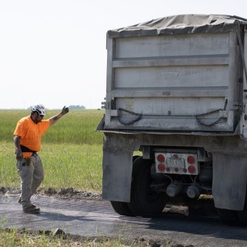 Construction worker directing dump trunk reversing into position