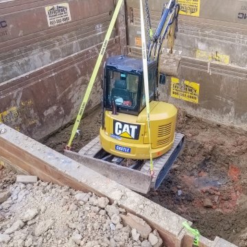 CAT yellow excavator lowered in utilities pit