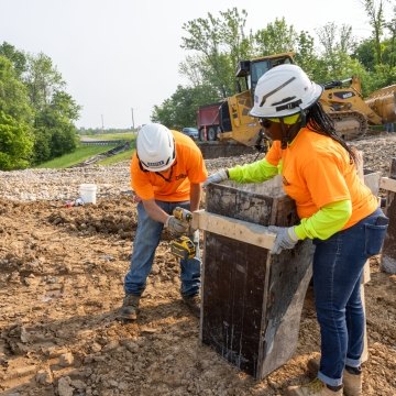 Woman construction worker holding wood panels together and man construction worker drilling wood through wood panels