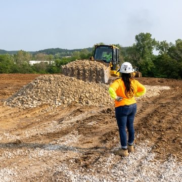 Woman construction worker watching bulldozer move rock pile