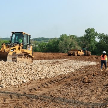 Woman construction worker walking past bulldozer moving rock pile