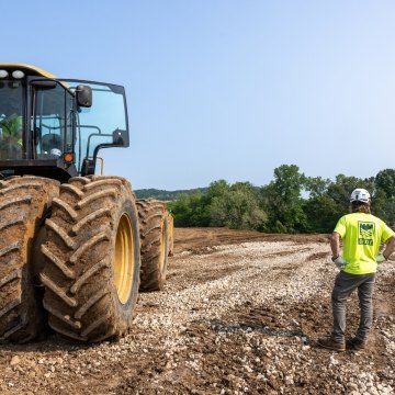 Castle Contracting construction worker next to large yellow tractor looking out across construciton site landscape
