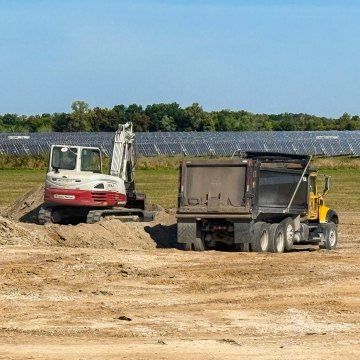 Dump truck and excavator facing solar panels in field