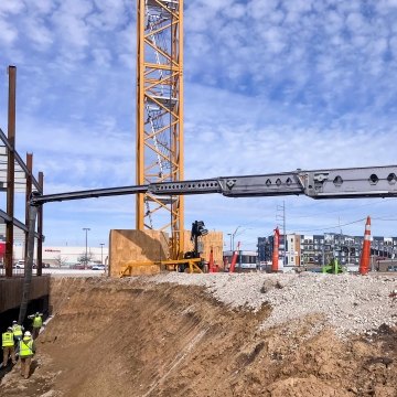 Workers in pit pouring concrete next to building foundation with crane tower in background