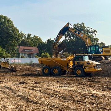 Mini dozer with CAT excavator dropping dirt into yellow John Deer dump truck
