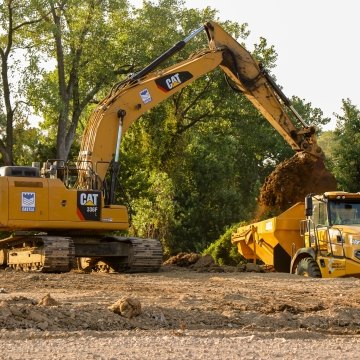 Yellow CAT excavator pouring dirt into yellow dump truck bed
